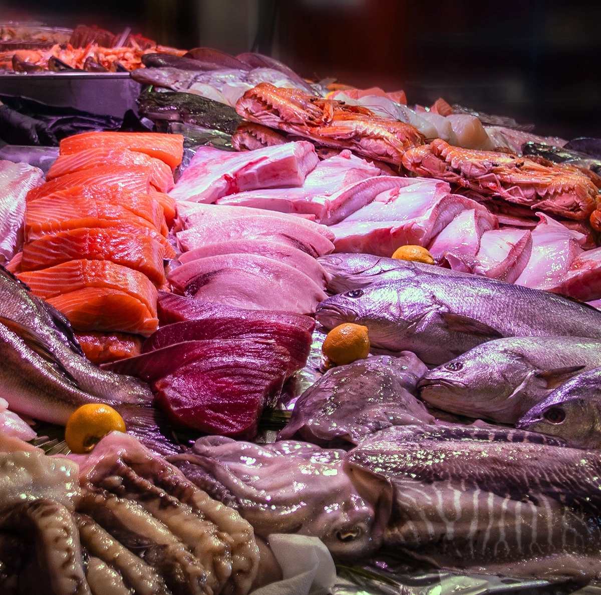 Assorted fresh seafood on display at a market, including salmon fillets, whole fish, and lobsters with lemons nearby.